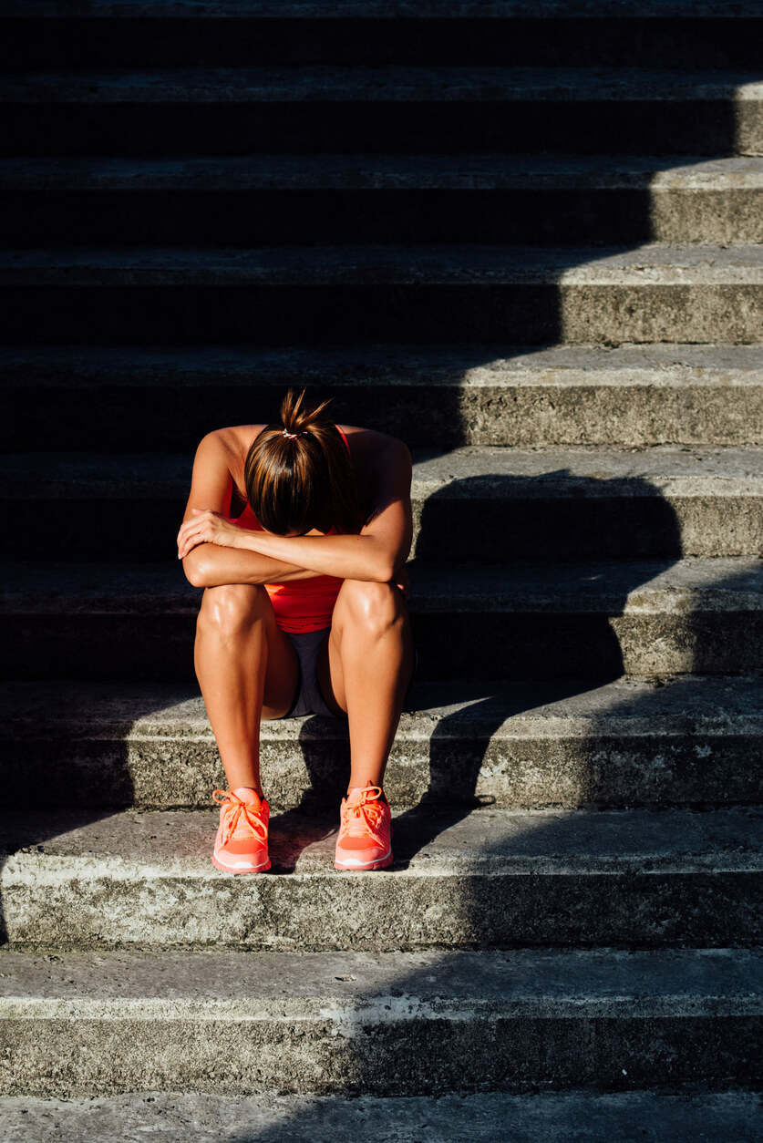 Female athlete sitting on steps with her head down, hunched over
